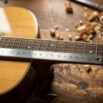 Pourquoi les cordes d’une guitare frisent-elles après leur remplacement ? Gros plan d’une guitare acoustique en bois posée sur l’établi d’un luthier, avec des cordes neuves et une règle près de la douzième frette.