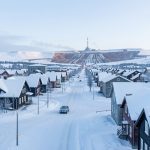 Comment Kiruna déplace-t-elle sa ville menacée par la mine de fer ? Vue panoramique hivernale réaliste de Kiruna en Laponie suédoise, avec un ancien quartier enneigé et une mine de fer visible au loin sous une lumière arctique froide.